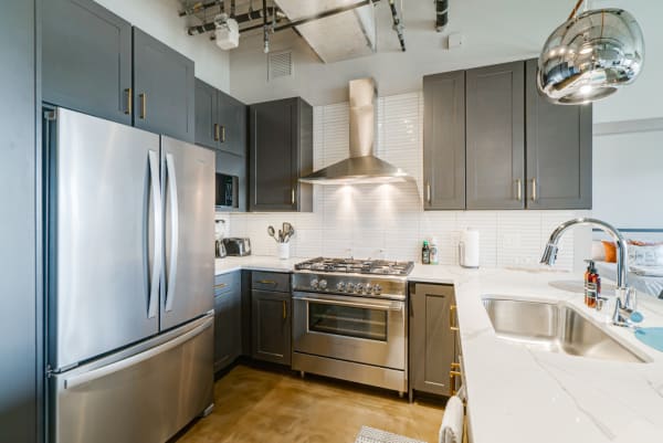 Sleek kitchen with gray cabinets, stainless steel fridge, gas range, and marble countertop.