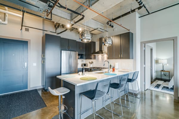 Modern kitchen with dark cabinetry and stainless steel appliances, featuring a kitchen island with bar stools.