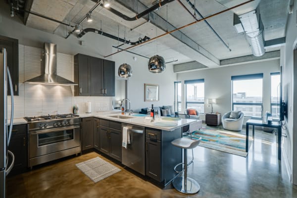 A modern kitchen with dark cabinets and polished concrete flooring, adjacent to a cozy living area with large windows.