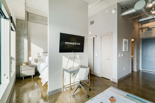 Interior view of a modern studio apartment with a bed, desk, and TV.