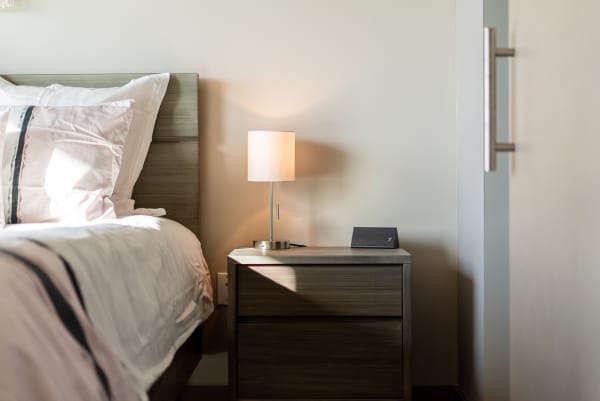 A serene bedroom featuring a bed with pink bedding, a modern lamp, and a speaker on the nightstand.