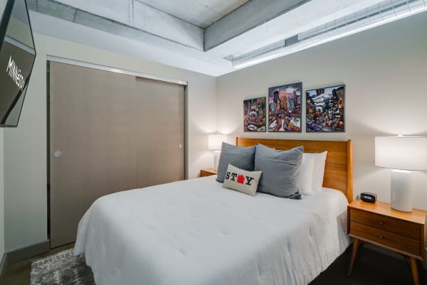 A modern bedroom featuring grey pillows, city artwork, and a white quilt.