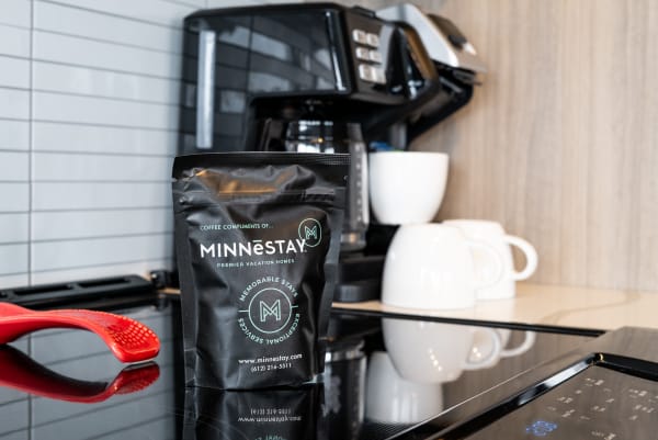 A coffee bag labeled 'MINNESTAY' in a contemporary kitchen with a coffee maker and white cups.