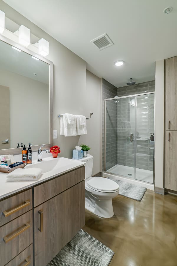 Modern bathroom with light wood vanity, white towels, and glass shower.