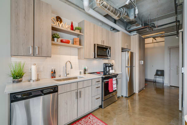 Modern kitchen featuring light wood cabinetry, stainless steel appliances, and decorative shelves.