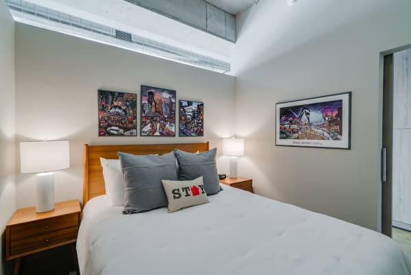 Modern bedroom with wooden bed, decorative pillows, and colorful artwork.