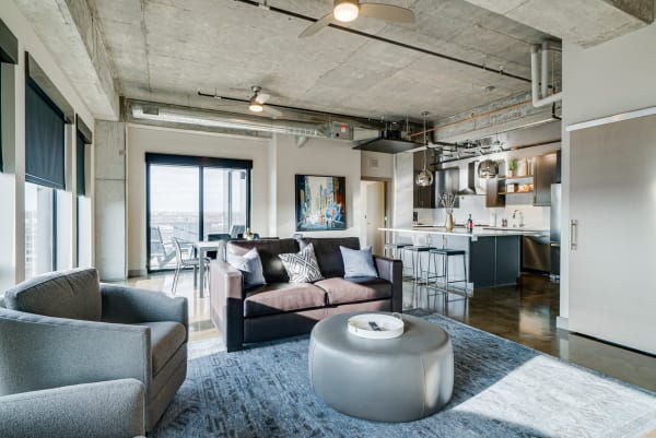 Modern urban apartment interior featuring a living area with a leather sofa, armchair, and a view from large windows.