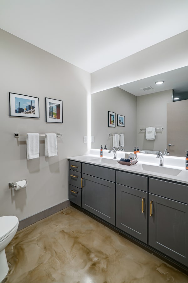 Modern bathroom with a double vanity, framed art on the walls, and polished concrete flooring.