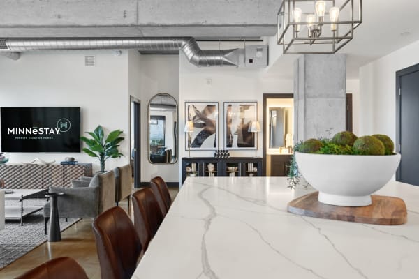 A contemporary kitchen and living space with a marble countertop, leather stools, and modern decor.