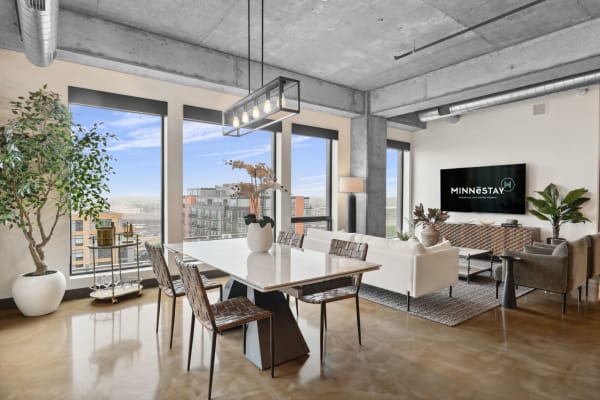 Modern apartment interior with dining area and living room, featuring large windows and stylish decor.