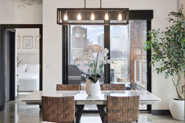 Modern dining space featuring a table, woven chairs, and a view of a rainy city through glass doors.