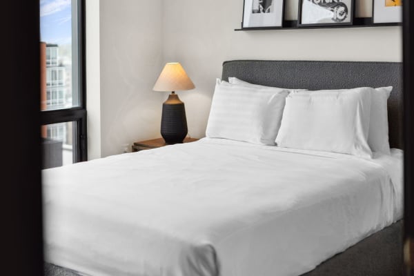 A cozy bedroom with a white bed, textured headboard, and black lamp.