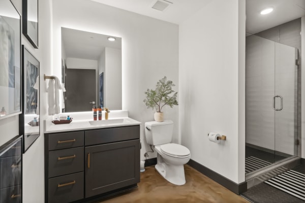A sleek bathroom with a backlit mirror, gray cabinetry, and a shower area.