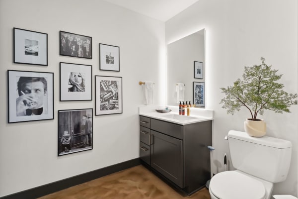 Modern bathroom with a dark vanity, illuminated mirror, and framed black-and-white photos on the wall.