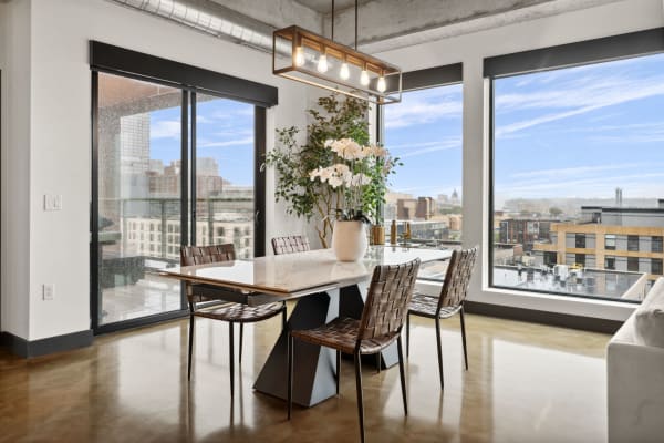 Modern dining area with a marble table and brown leather chairs, featuring large windows and urban views.