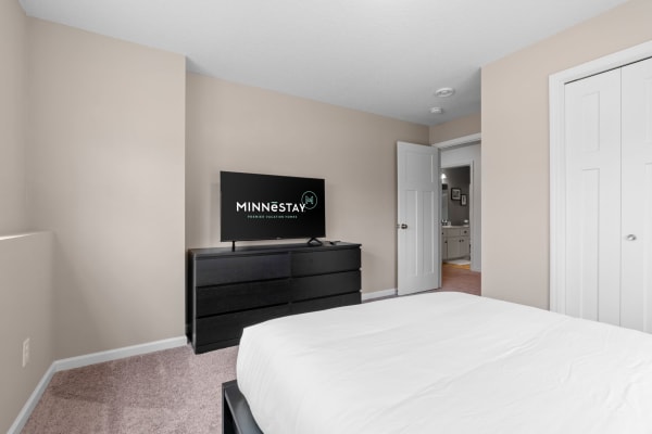 Contemporary bedroom with a black dresser and flat-screen TV, leading to a bathroom.