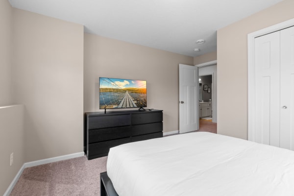 A modern bedroom featuring a bed, dresser with a TV, and an open door leading to a bathroom.