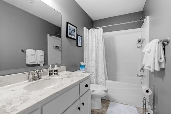 Modern bathroom with marble countertop, gray walls, and floral shower curtain.
