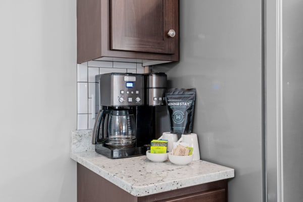 A stylish coffee station with a coffee maker, tea bags, and sweeteners on a granite countertop.