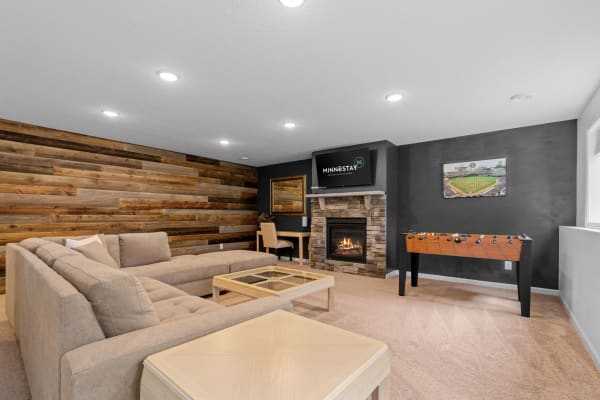A modern living room featuring a beige sectional sofa, stone fireplace, and foosball table.