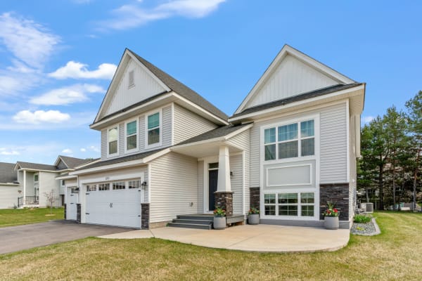 Exterior view of a modern two-story house featuring stone accents and a vibrant garden, under a clear blue sky.