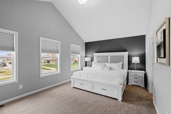 A modern bedroom with a white bed, gray walls, and natural light coming from windows.