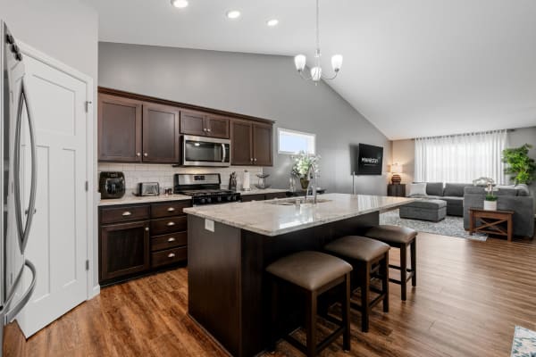 Modern kitchen with dark cabinets and open living area featuring a gray sectional sofa.