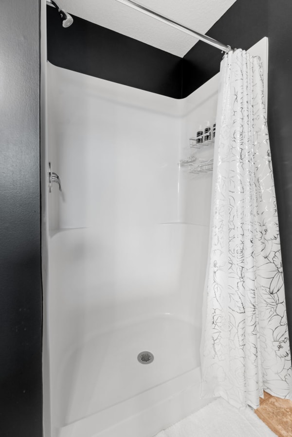 A sleek shower with white tub and wall, decorative floral curtain, and black backdrop.