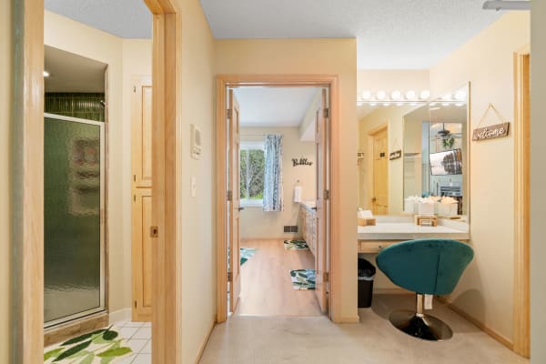 A spacious bathroom with modern fixtures, including a glass shower and a teal vanity chair.