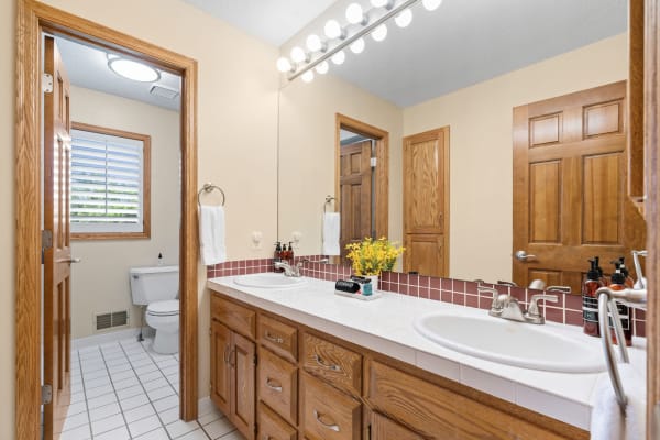 Interior view of a cozy bathroom with double sinks, wooden cabinets, and yellow flowers.