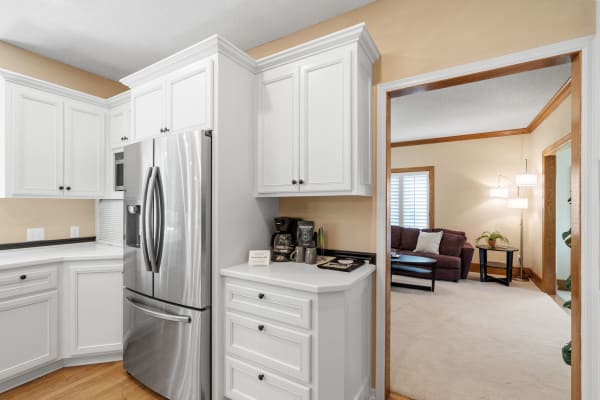 Modern kitchen with white cabinets and stainless-steel refrigerator, leading to a cozy living area.