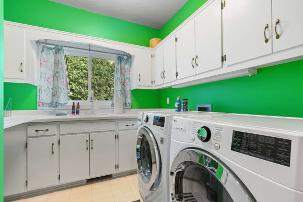 Laundry room featuring green walls, modern washing machines, and white cabinets.