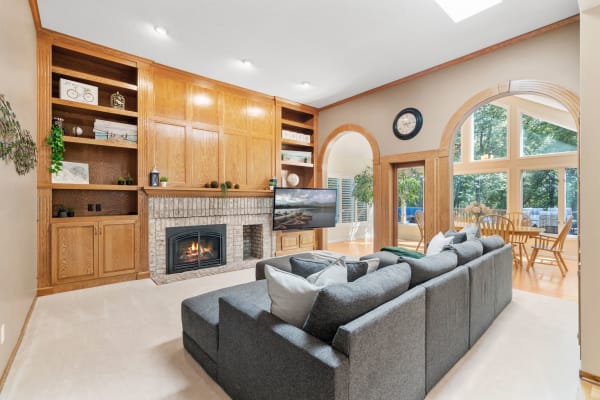 Modern living room with gray sectional sofa, brick fireplace, and large windows.