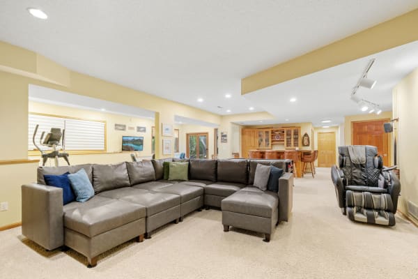 A spacious basement with a sectional sofa, workout equipment, and a home bar.