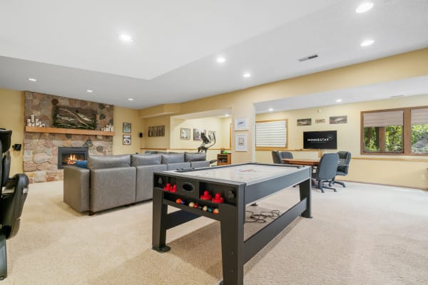 Interior view of a basement recreation room with a fireplace, sectional sofa, and air hockey table.