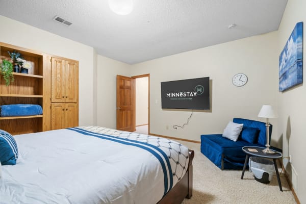 A cozy bedroom with a queen bed, armchair, and wall-mounted television.