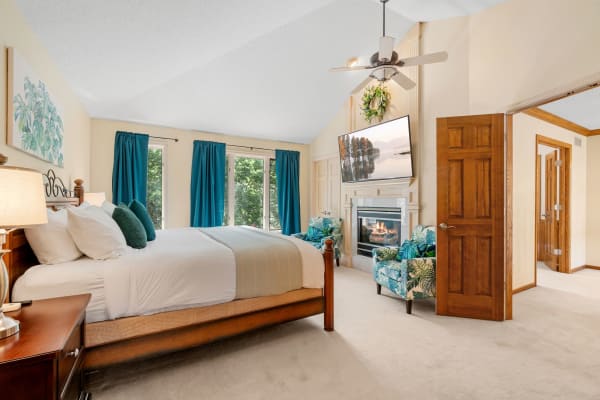 A spacious bedroom with a large bed, a TV mounted over a fireplace, and tropical-themed furniture.