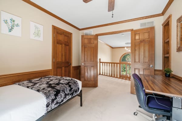 Cozy bedroom with a bed, desk, and wooden accents, opening to a hallway.