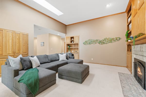 Interior of a living room with a gray sectional sofa, fireplace, and wooden cabinets.