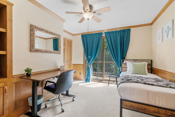 A cozy bedroom with a metal bed, teal curtains, and a wooden desk.