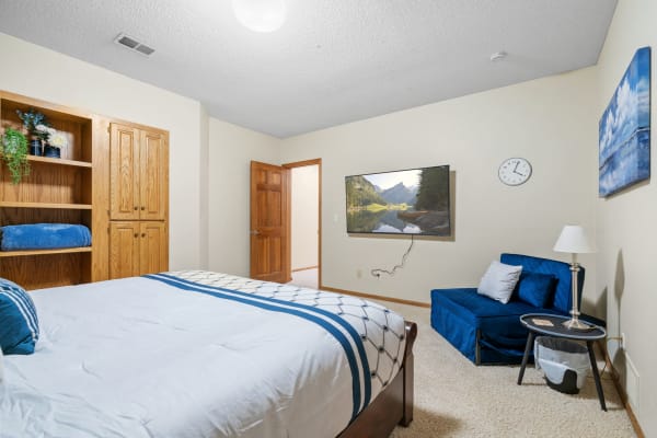 A modern bedroom featuring a neatly made bed, TV, and cozy seating.