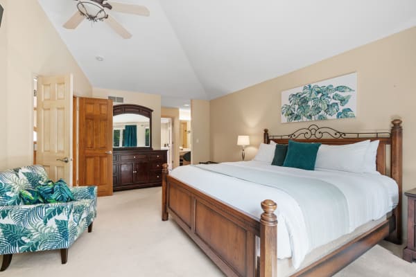 Spacious bedroom with a wooden bed, tropical patterned armchair, and high ceiling fan.