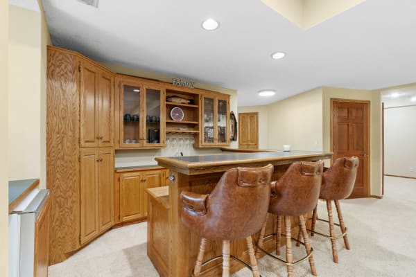 Cozy home bar area featuring wooden cabinets and leather stools.