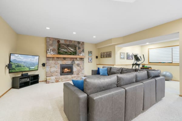 A stylish basement living room with a stone fireplace, sectional sofa, and fitness area.