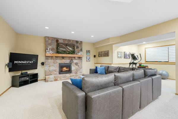A stylish basement living room featuring a stone fireplace, gray sectional sofa, and entertainment setup.