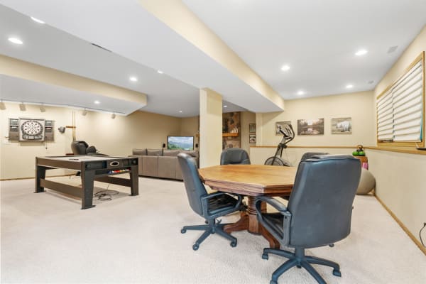 A spacious basement recreational area featuring a round table, air hockey table, and sectional sofa.