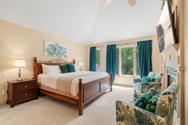 A cozy bedroom featuring a wooden bed, teal curtains, and tropical-themed chairs.