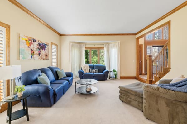 A spacious living room with blue sofas, a round coffee table, and large windows overlooking greenery.