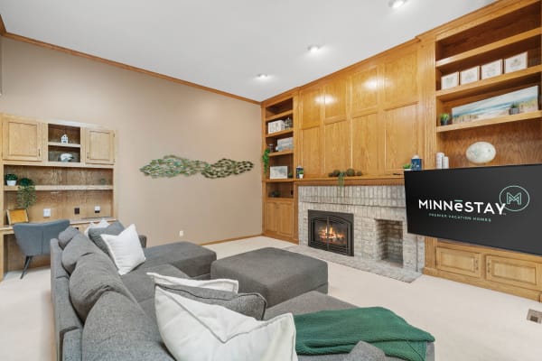 Cozy living room with a grey sofa, brick fireplace, and wooden shelves.
