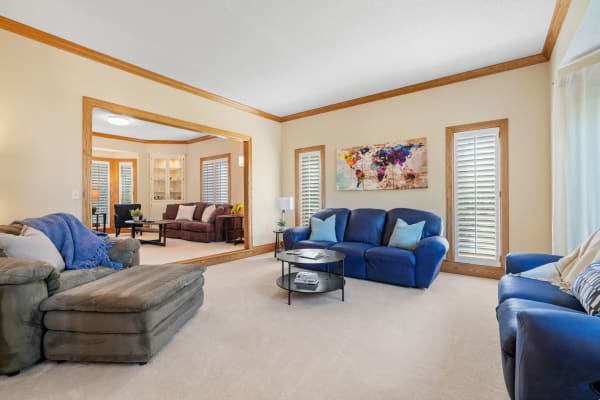 A spacious living room featuring a blue couch, green fabric sofa, and brown sectional, with a colorful abstract map painting on the wall.